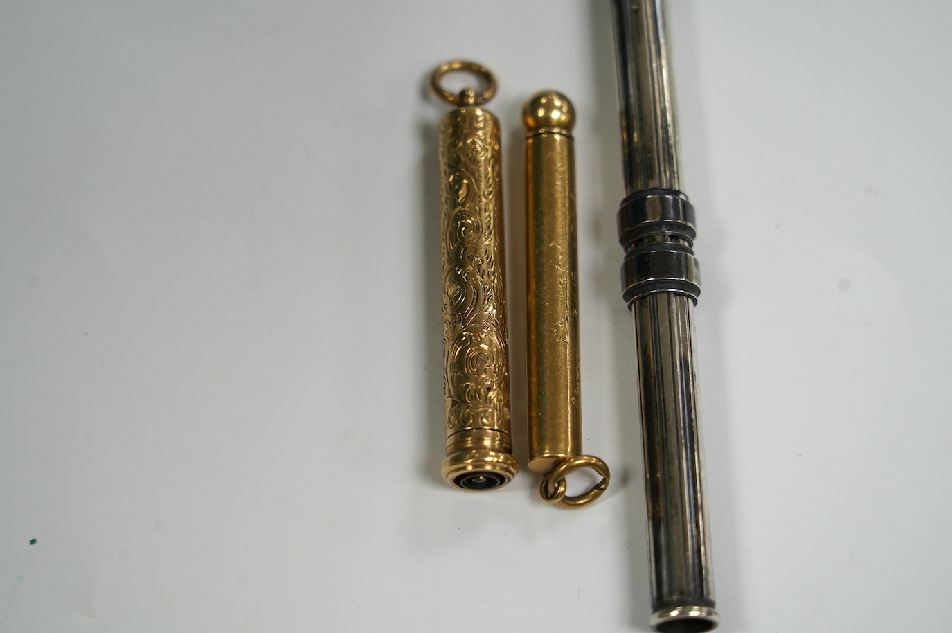 Two yellow metal overlaid propelling pencils, including late Victorian with engraved inscription, 54mm and one other silver cased propelling pencil and pen combination, 10cm long when closed. Condition - fair